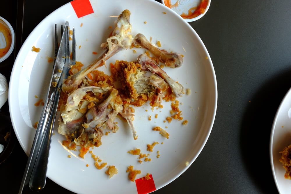 chicken-bones-with-some-breading-on-a-white-plate-beside-silverware