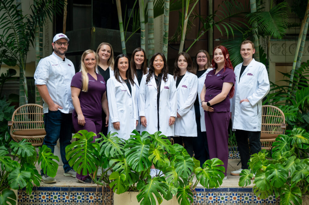 Members of Ollie's science team posing together indoors in front of lush tropical plants and a tiled planter wall.