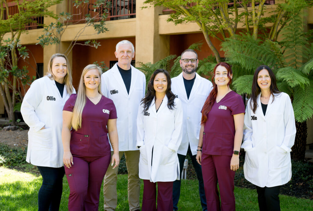 A group portrait of veterinarians and veterinarian technicians in white lab coats and purple scrubs.